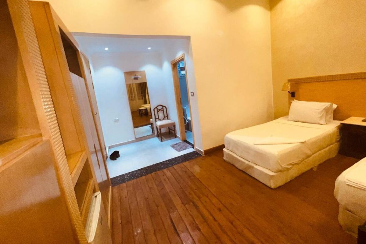 Ein kleines Hotelzimmer mit Holzboden, einem Bett, einem Nachttisch und einem Sessel.