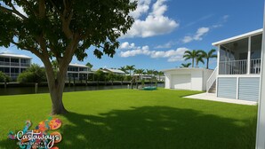 A residential area with a large tree, a grassy lawn, and a house with a balcony. - Blue Heron is your waterfront 3BR/2BA getaway with boat lift, huge seawall (St James City)