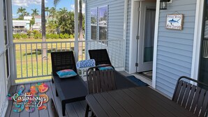 A covered outdoor seating area with two chairs and a table, a sign encouraging more tourists, and a view of the yard with palm trees. - Blue Heron is your waterfront 3BR/2BA getaway with boat lift, huge seawall (St James City)