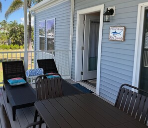 Un espace extérieur abrité avec deux chaises et une table, une pancarte encourageant davantage de touristes à venir, et une vue sur la cour avec ses palmiers.