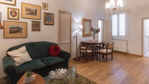 Een woonkamer met een groene bank, een bijzettafeltje met een plant en een eethoek met een tafel en stoelen.