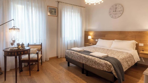 Hotelkamer met een houten bed, een nachtkastje met een lamp, een stoel en een klein tafeltje met dienblad en theepot.