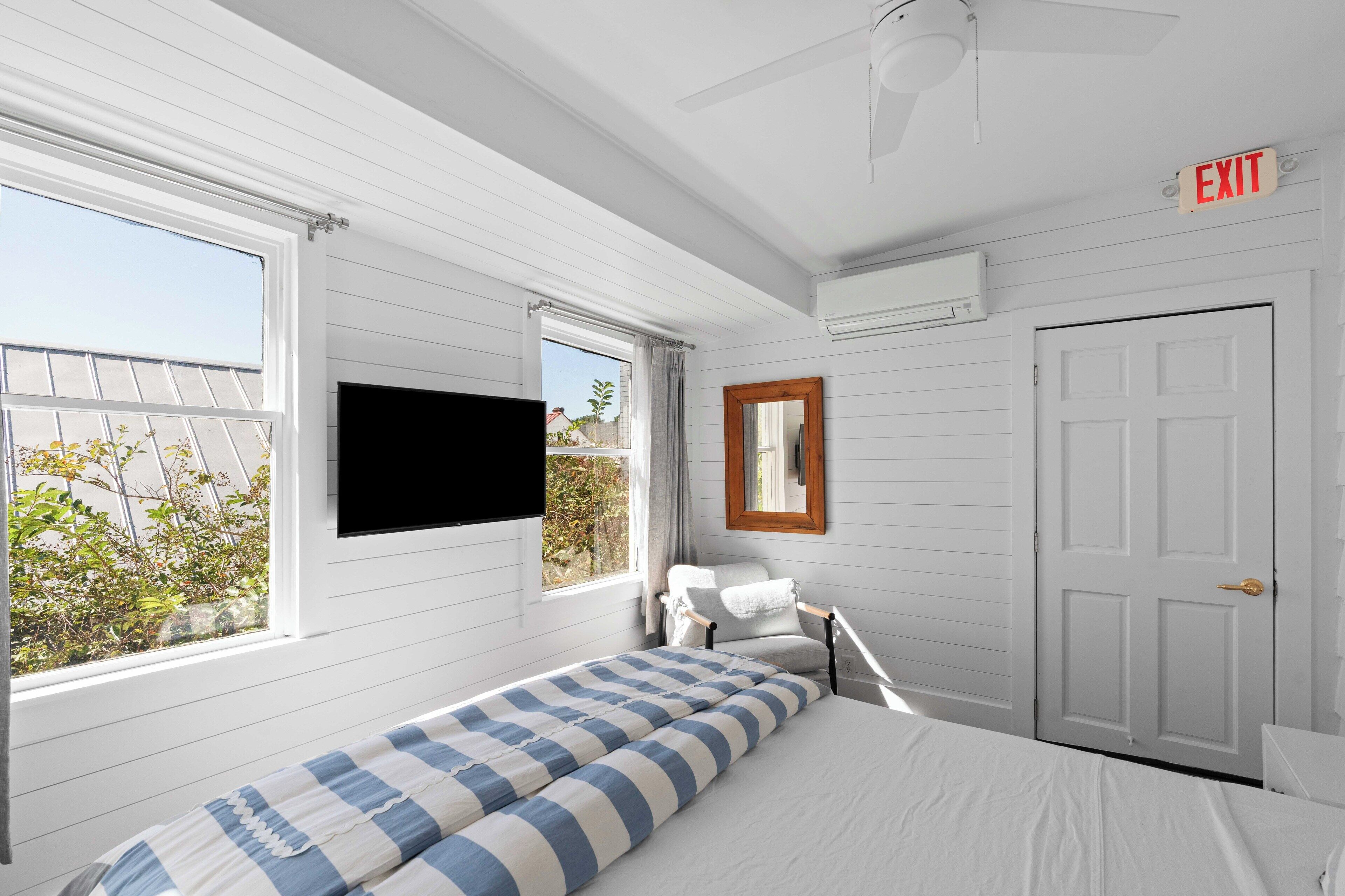 A room with a bed, a chair, a TV, and an exit sign.