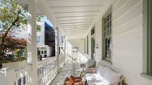 A covered porch with white railings, wicker furniture, and a table with a bottle. - Luxe 5BR w/ Heated Pool~1 Block to King~Lowcountry House (Charleston)