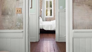 A hallway with a wooden floor, white walls, and a mural of trees. There is a door leading to a room with a bed and a window. - Luxe 5BR w/ Heated Pool~1 Block to King~Lowcountry House (Charleston)