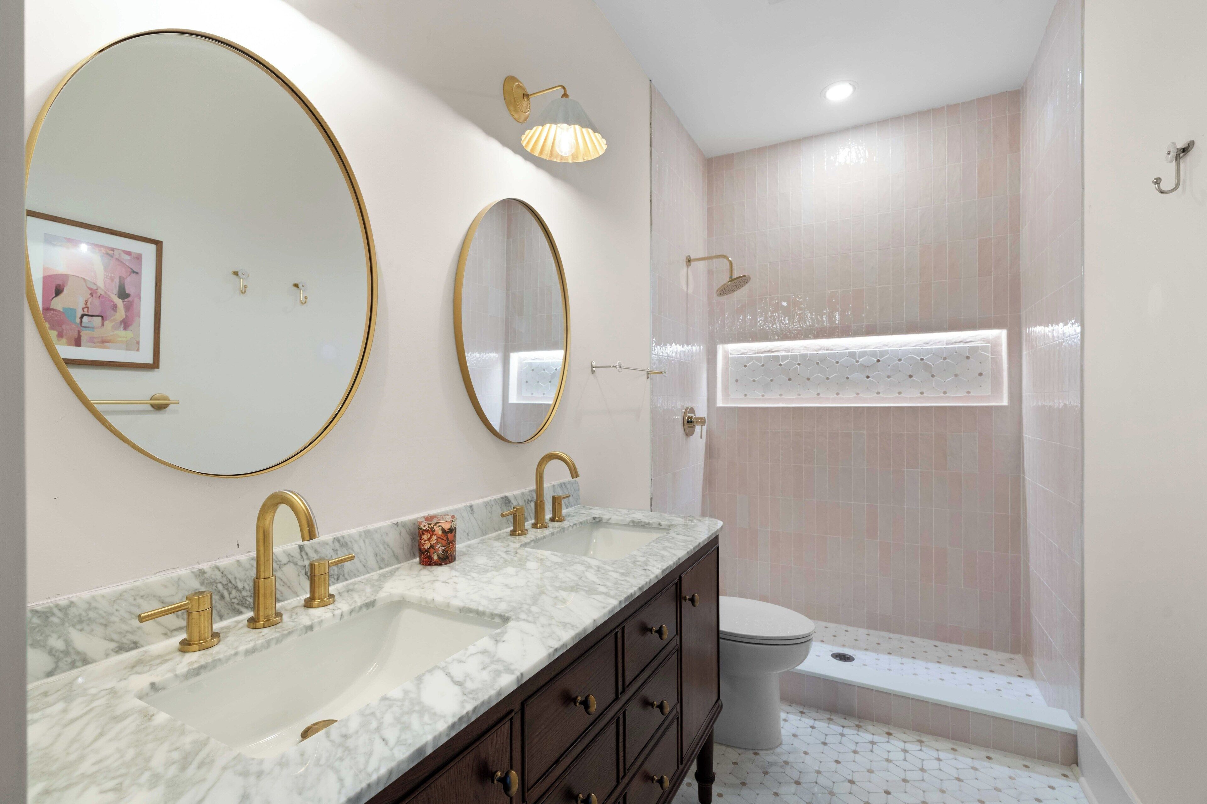 A bathroom with a marble vanity, two gold-framed mirrors, a white toilet, and a shower with a glass door.