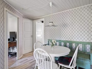 A room with a round table, white chairs, a bench with a green backrest, and patterned wallpaper. - 4 Star Holiday Home in Bergshamra (Bergshamra)