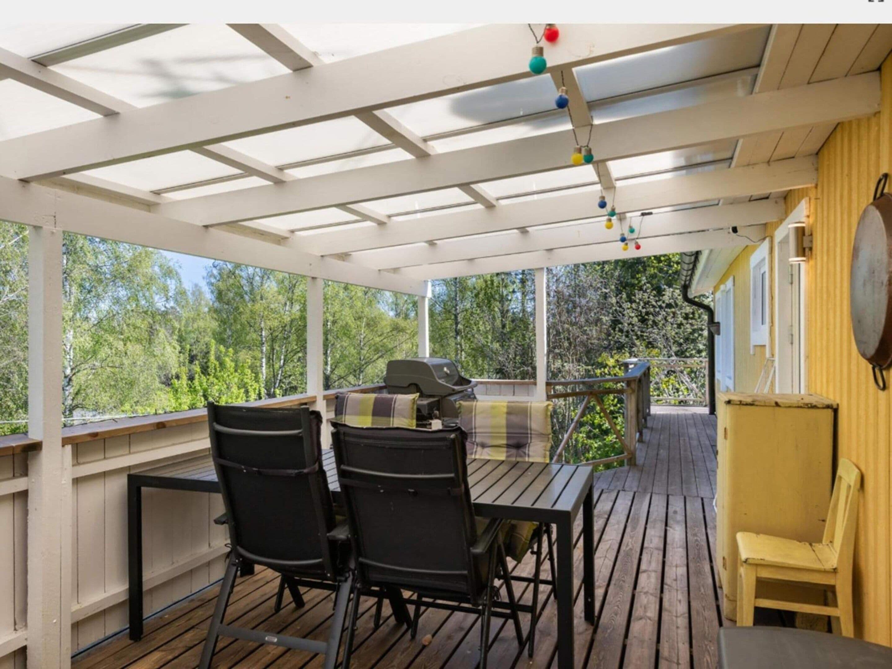 A covered outdoor area with a table and chairs, a grill, and a view of trees.