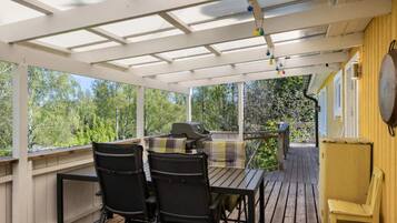 A covered outdoor area with a table and chairs, a grill, and a view of trees.