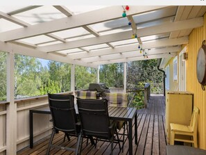 A covered outdoor area with a table and chairs, a grill, and a view of trees. - 4 Star Holiday Home in Bergshamra (Bergshamra)
