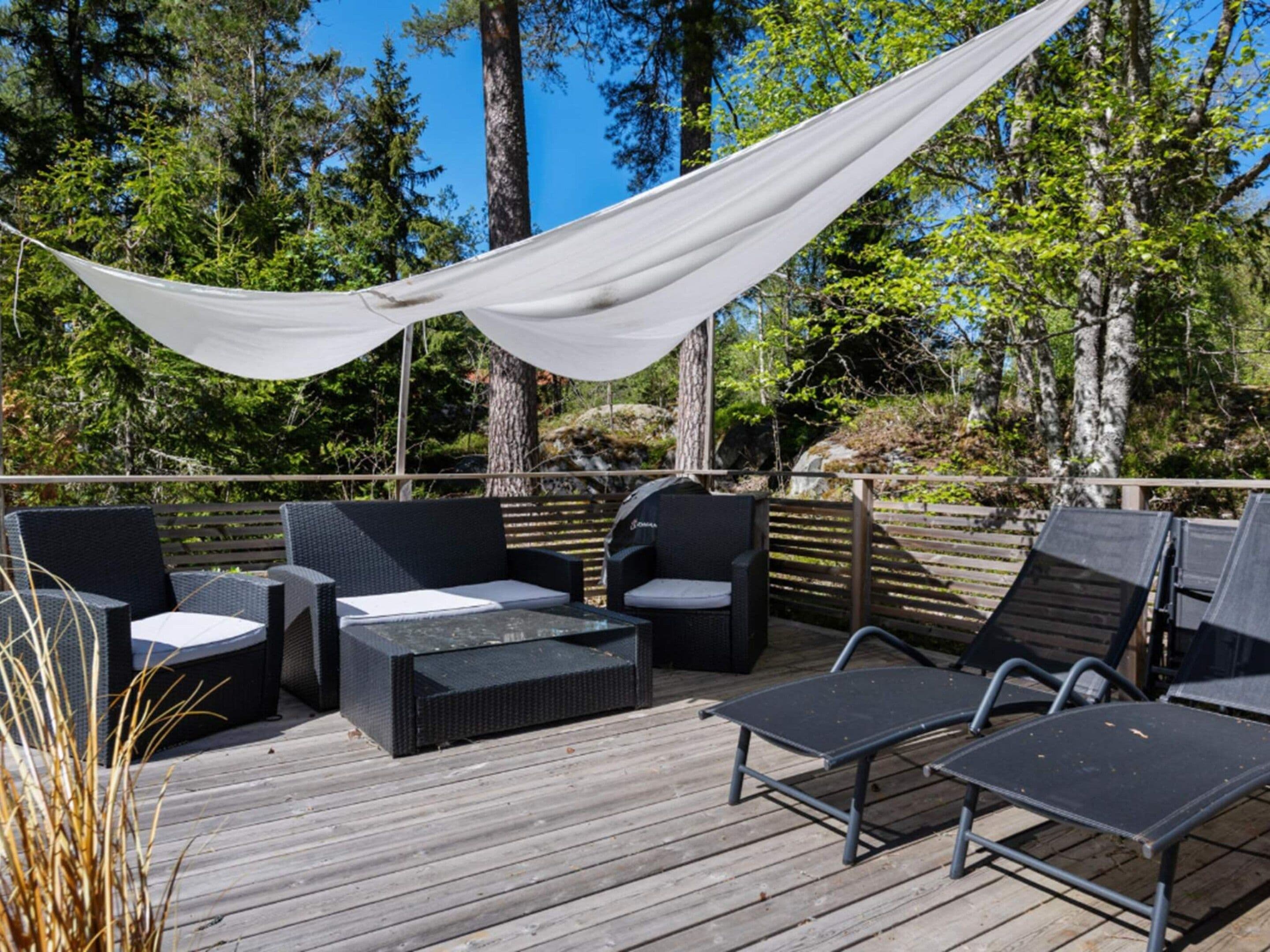 Una terraza exterior con mobiliario de mimbre, una parrilla y un toldo.