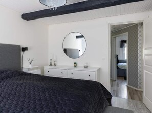 A bedroom with a large bed, a white dresser, a round mirror, and a door leading to another room. - 4 Star Holiday Home in Bergshamra (Bergshamra)