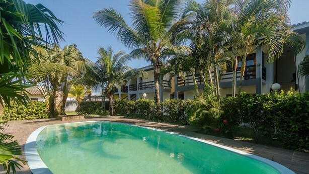 A swimming pool surrounded by palm trees and a building with balconies. - Fully Equipped Apartments in Condo With Pool 500m From Taperapua Beach - Enls (Porto Seguro)