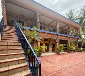 Ein zweigeschossiges Haus mit überdachter Veranda, einer Treppe und Blumentöpfen.