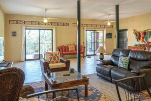 A spacious living room with a leather sofa, a patterned armchair, and a glass coffee table. - GARDEN – 2BR Treetop Home Steps from Los Ayala Beach (Los Ayala)