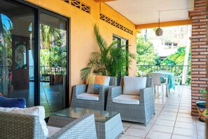 A covered outdoor seating area with wicker furniture, a glass door leading to a patio, and a view of a residential area.