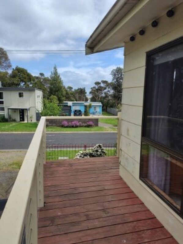 A building with a wooden deck, a large window, and a view of a street with houses and greenery. - Grantville Stay Comfy Home, Near Beaches and Phillip Island (Grantville)