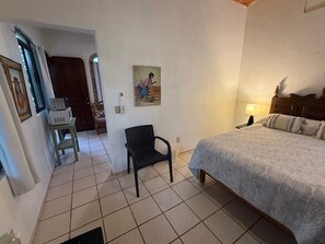 Een slaapkamer met een bed, een stoel, een schilderij en een deur die naar een andere kamer leidt.