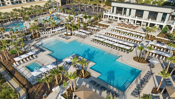 Eine Luftaufnahme eines Resorts mit mehreren Schwimmbecken, Liegestühlen und Palmen.