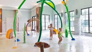 Ein Indoor-Wasserparadies mit verschiedenen Wasserspielen, darunter eine große Bogenkonstruktion und eine pilzförmige Fontäne.
