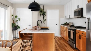 A modern kitchen with white cabinets, a central island, wooden flooring, and a black pendant light.