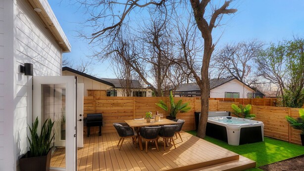 A wooden deck with a table and chairs, surrounded by a wooden fence and a tree.