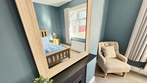 Ein Zimmer mit einem Bett, einem Sessel, einem Kamin und einem großen Spiegel.