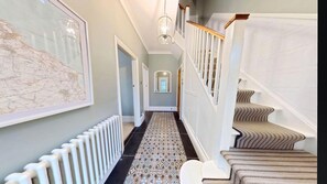 A hallway with a patterned carpet, a radiator, a staircase with a patterned carpet, and a hanging light fixture. - Peasholm Place -  a cottage that sleeps 8 guests  in 5 bedrooms (Scarborough)