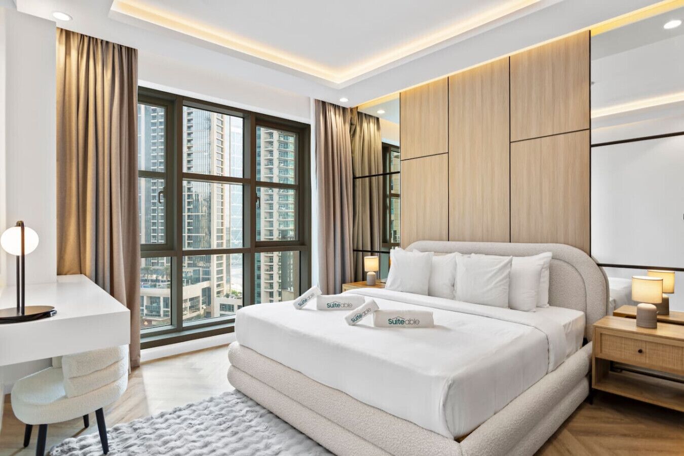 A modern hotel room with a large bed, a desk, and a view of high-rise buildings.