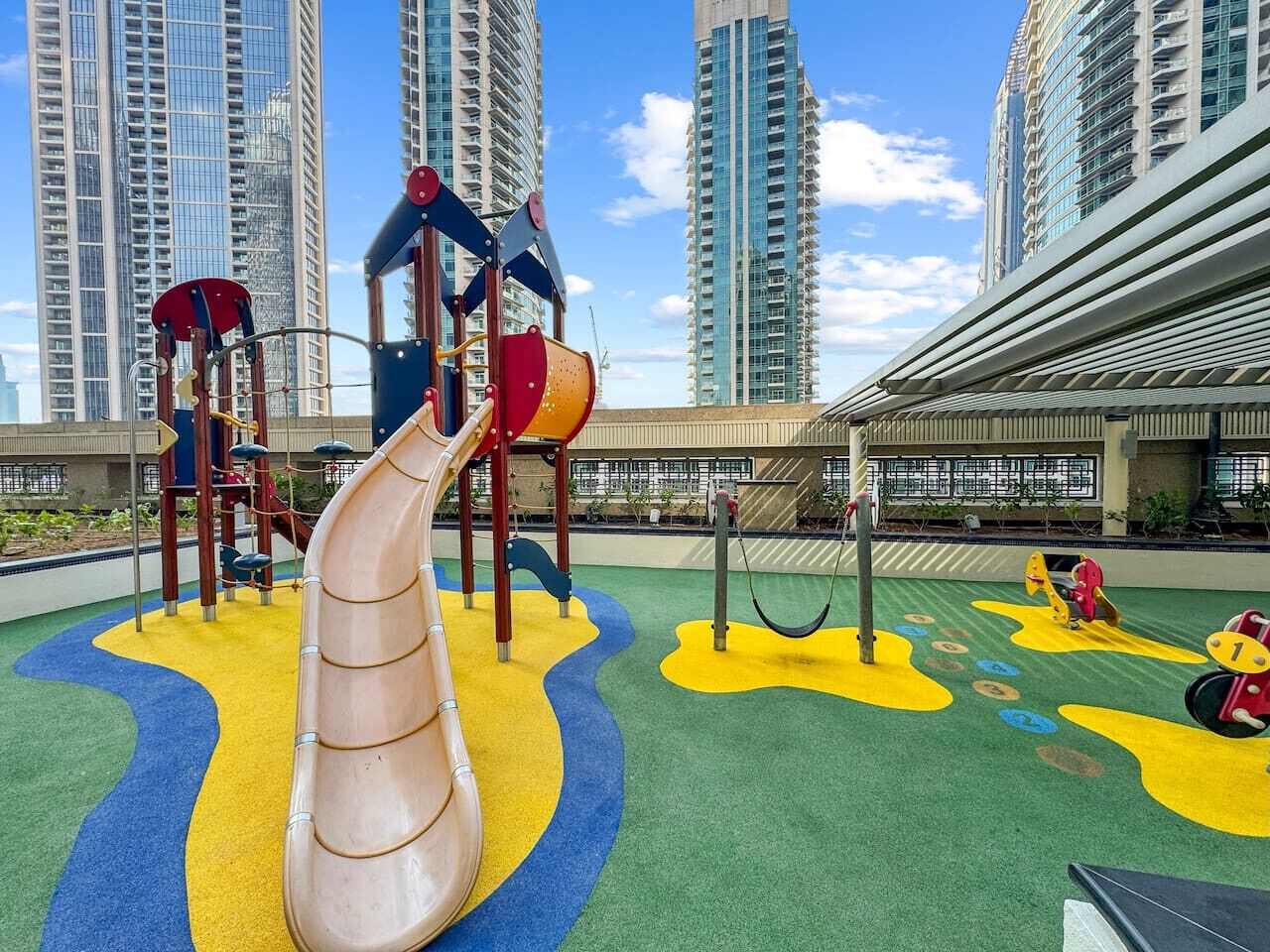 Um parquinho com escorregadores e estruturas de escalada, cercado por edifícios altos.