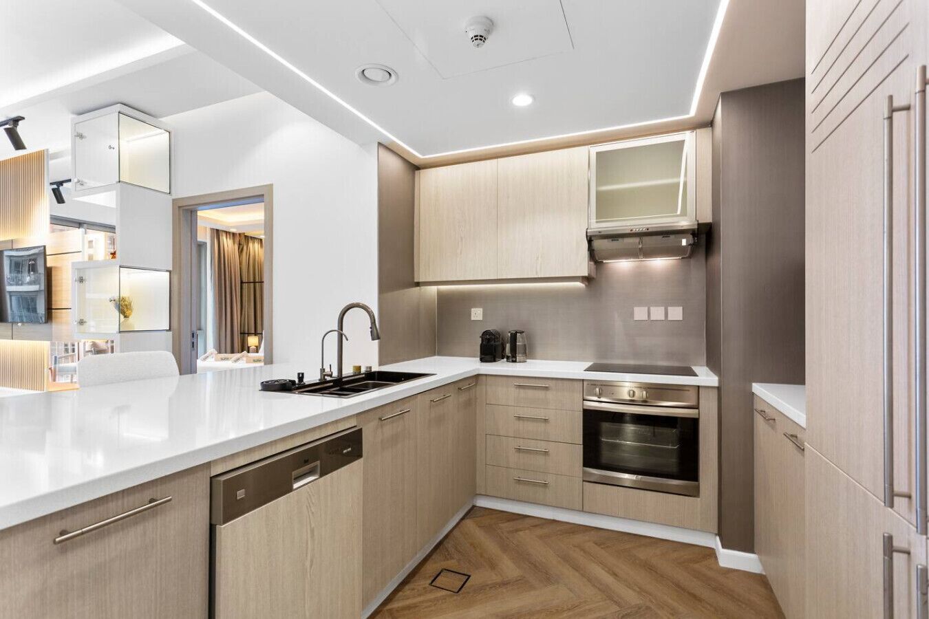 Een moderne keuken met lichte houten kastjes, roestvrijstalen apparatuur en een wit aanrecht.