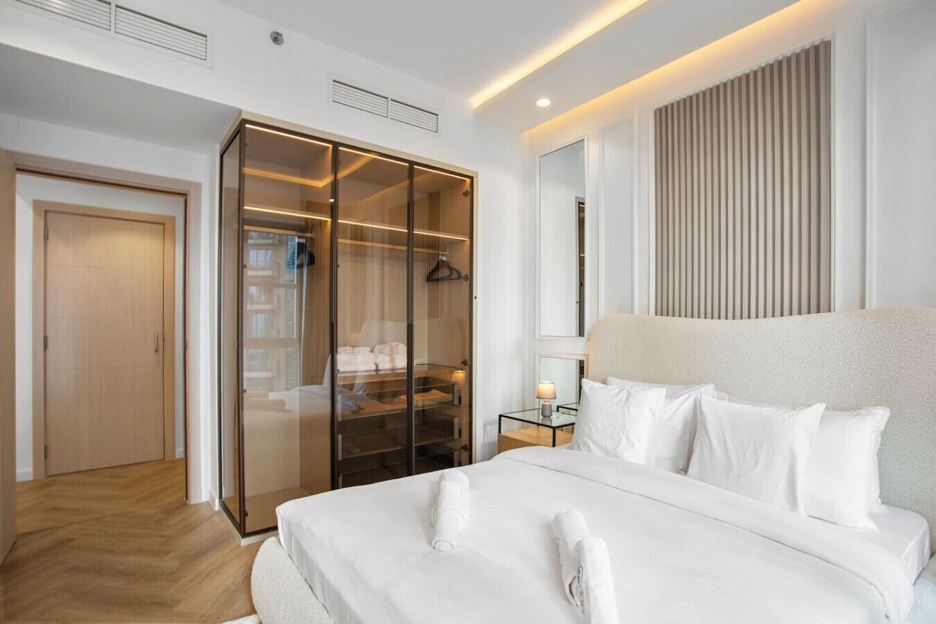 Una habitación de hotel moderna con una cama grande, un vestidor amplio y un ventanal con persianas.