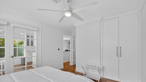 A bedroom with a bed, a ceiling fan, a white wardrobe, and a view of the kitchen. - Charming 2-bedroom bungalow in lovely Delray Beach with AC (Delray Beach)