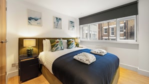 Una camera da letto ordinata con un letto, un comodino e una finestra che si affaccia su edifici.