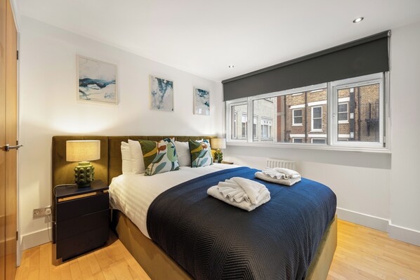 A neatly arranged bedroom with a bed, bedside table, and a window with a view of buildings.