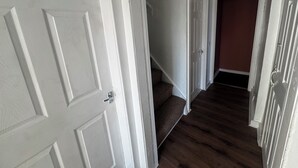 A hallway with a white door, a staircase, and a dark wooden floor. - Spacious 4BR Home Near Edinburgh Airport and City Centre – Parking (Edinburgh)