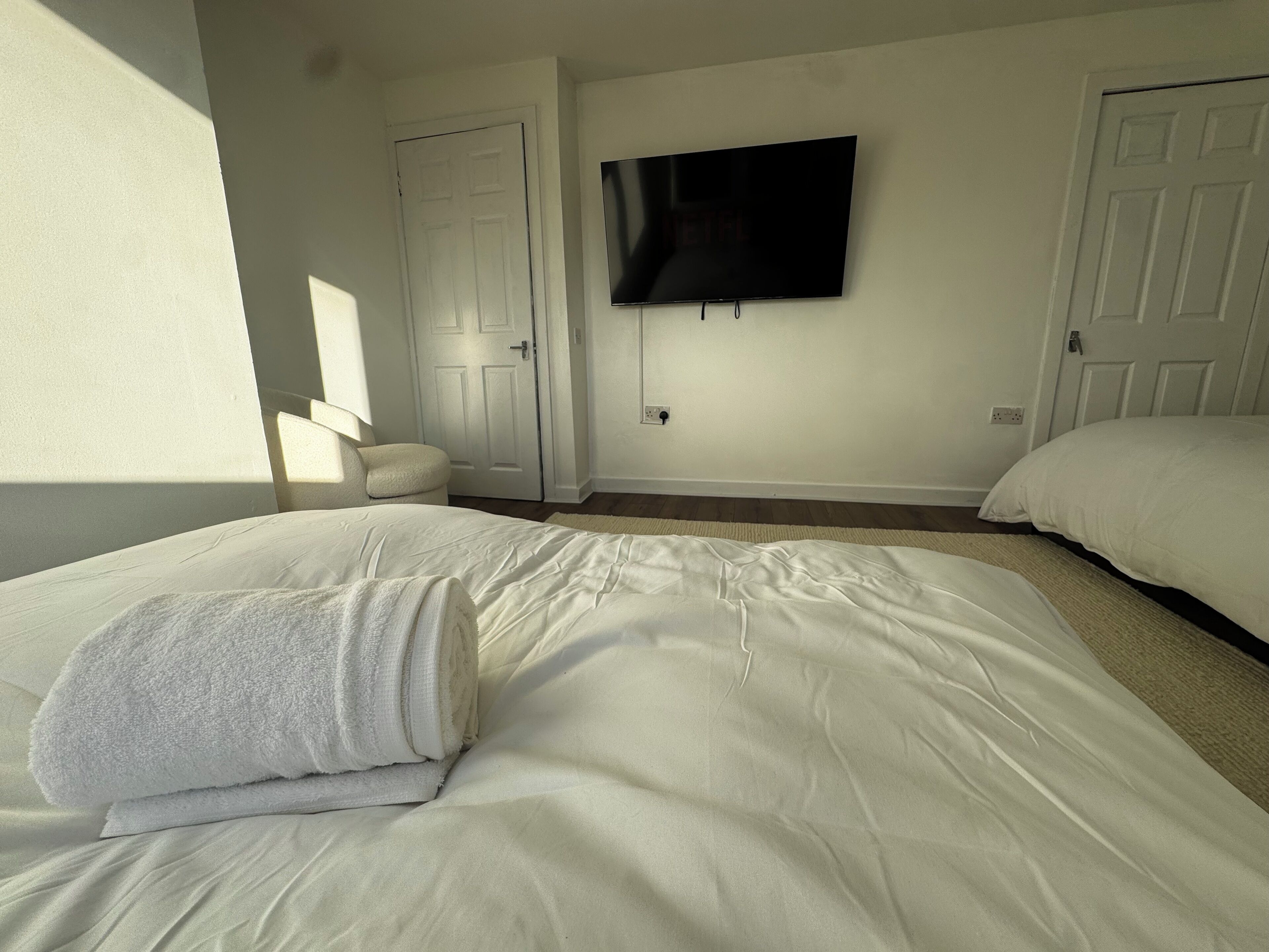 Una camera da letto con due letti, una TV a schermo piatto montata a parete e una porta sullo sfondo.