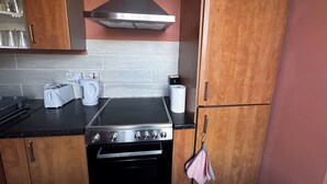 A kitchen with wooden cabinets, a stainless steel range hood, a built-in oven, a toaster, a kettle, and a roll of paper towels. - Spacious 4BR Home Near Edinburgh Airport and City Centre – Parking (Edinburgh)