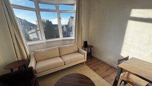 A living room with a beige sofa, a round wooden coffee table, a small wooden side table, and a dining table with chairs. - Spacious 4BR Home Near Edinburgh Airport and City Centre – Parking (Edinburgh)