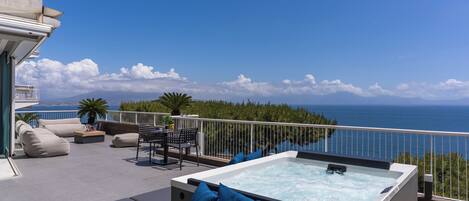 A rooftop terrace with a hot tub, outdoor seating, and a view of the ocean.