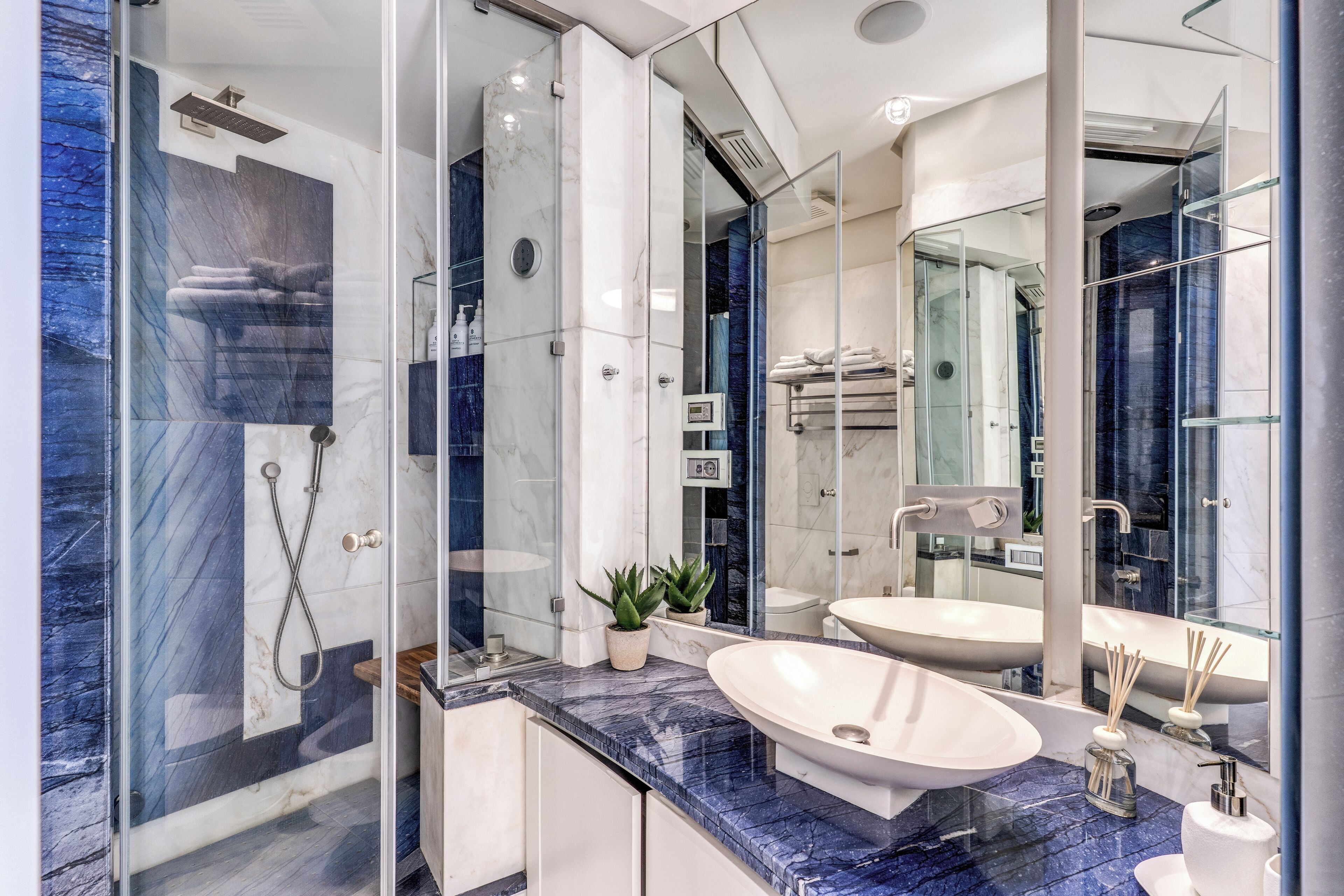 Un baño moderno con ducha de vidrio, encimera de mármol y un espejo grande.