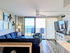 Un salon comprenant un canapé, des fauteuils, une table basse, un téléviseur et un balcon avec vue sur l’océan.