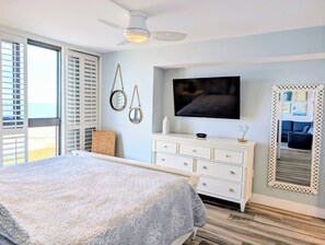 Un dormitorio con cama, televisor, cómoda y un espejo grande.