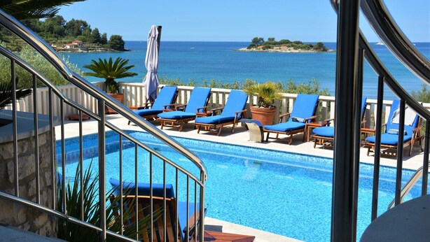 Une piscine avec des chaises bleues et vue sur la mer.
