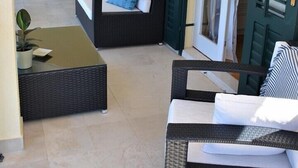 Un patio ensoleillé, aménagé avec des meubles en osier, notamment un canapé et un fauteuil, ainsi qu’une petite table sur laquelle est posée une plante en pot.