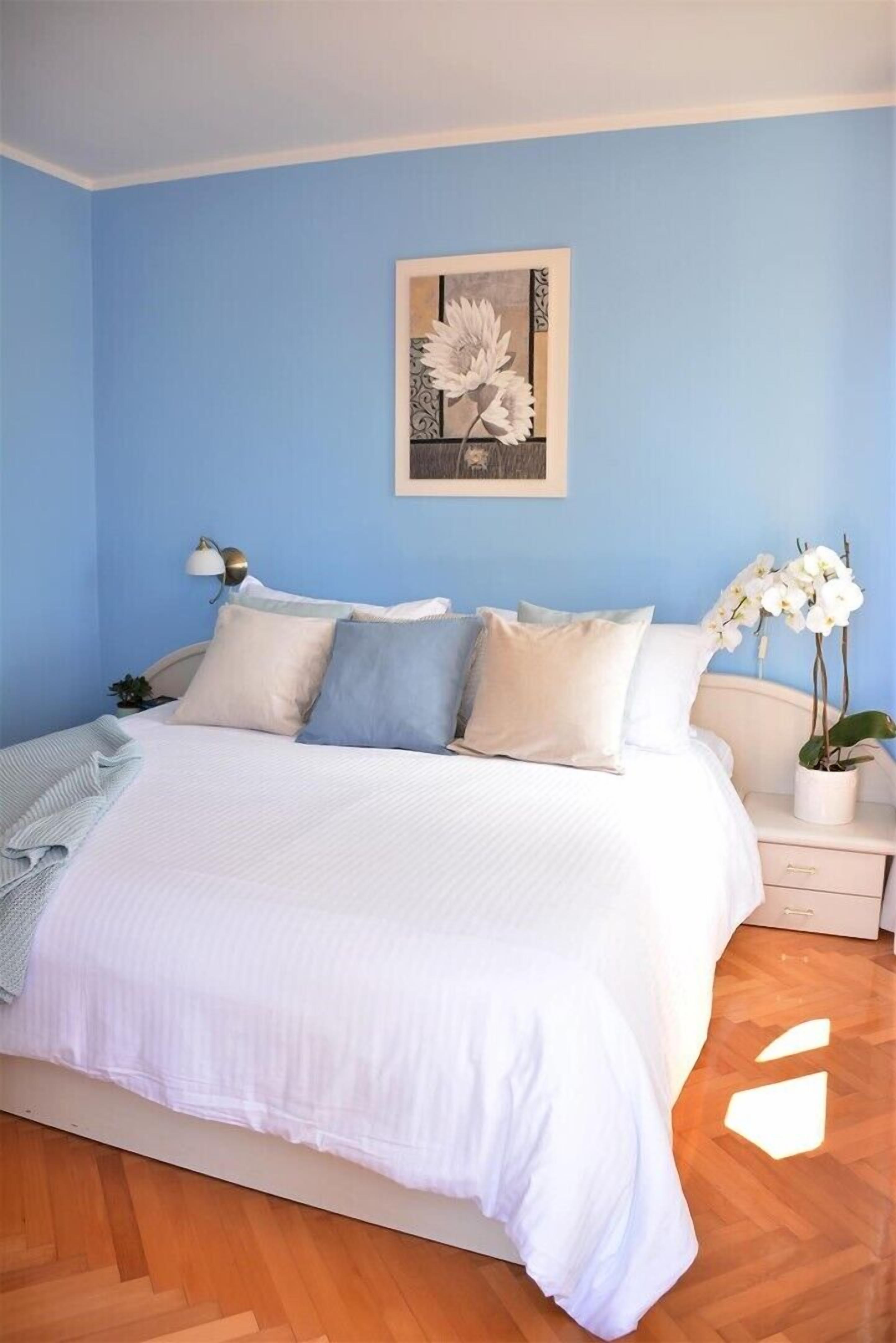 A bedroom with a large bed, a bedside table, a lamp, and a potted orchid.