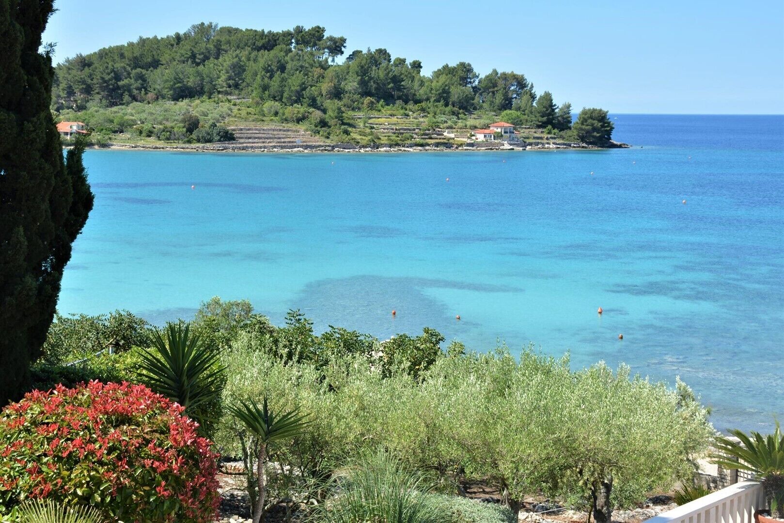 A coastal landscape with a clear view of the sea, a hill with trees, and a building in the background.
