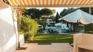 Een terras met buitenmeubilair, een zwembad en een overdeeld gedeelte met parasols.