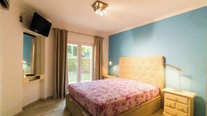 Een slaapkamer met een bed, nachtkastje, televisie bevestigd aan de muur en een raam met gordijnen.