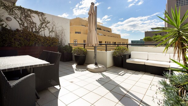 A rooftop terrace with a table and chairs, a sofa, potted plants, and an umbrella. - Chic Unit With Rooftop Terrace Near Sights & Shops (Sydney)
